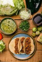 Marinated beef tacos, bowl with salsa verde and vegetables on a wooden table. Tacos de adobada.