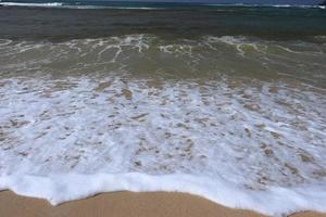 orilla del océano con playa de arena y olas que avanzan. espuma de agua con arena suave. hermosas olas en el fondo de la playa de arena. foto