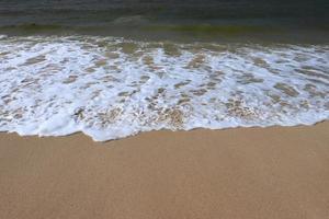 Ocean shore with sandy beach and advancing wave.  Water foam with smooth sand.  Beautiful waves on the sand beach background. photo