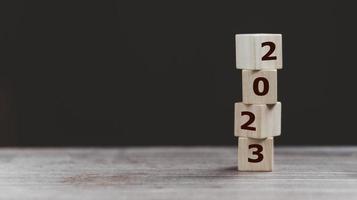 2023 Happy New year background banner. Two thousand Twenty-Three year numbers on wooden cube blocks stack on dark  background with copy space. Welcome, Merry Christmas, and Happy New Year in 2023. photo