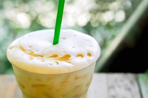 Ice Latte on a wooden terrace by the garden with sun flare and green leave background. Ice Latte is a popular drink in the summer of Thailand. photo