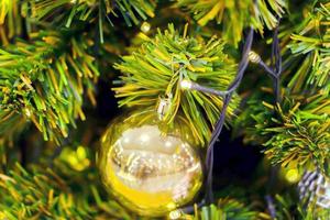 cierre las hojas de pino de plástico y la bola de navidad dorada con iluminación navideña en el fondo de pantalla completa. foto