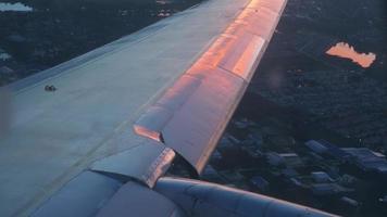 Plane flight above the city, sun glimpse over wing. Airplane sunrise flight. Traveling by air video