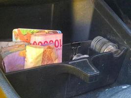 Some rupiah coins and one hundred thousand rupiah notes and some other money in a box provided on the dashboard of the car photo