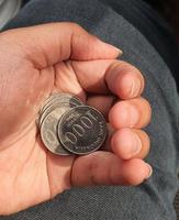 A hand is holding several rupiah coins. These coins are usually used to give to packs of people who help cross the vehicle or direct them to turn around. photo