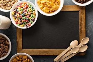 Variety of cold cereals in white bowls around chalkboard photo