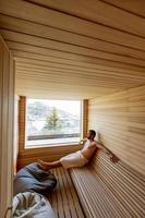 joven relajándose en la sauna y viendo el bosque de invierno a través de la ventana foto