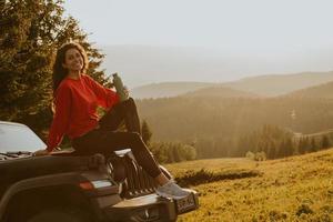 mujer joven relajándose en el capó de un vehículo de terreno en el campo foto