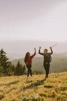 Smiling couple walking with backpacks over green hills photo