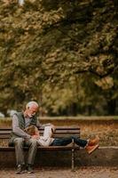 Grandfather spending time with his granddaughter on bench in park on autumn day photo