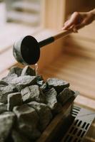 Hand of young woman pouring water on hot rocks in the sauna photo