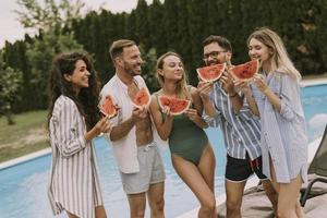 Young people standing by the swimming pool and eating watermelon in the house backyard photo