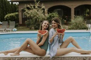Young women sitting by the swimming pool and eating watermelon in the house backyard photo