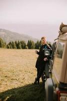 joven relajándose y bebiendo café junto al capó del vehículo del terreno en el campo foto