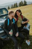 pareja joven relajándose en el capó de un vehículo de terreno en el campo foto