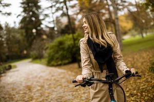 mujer joven con bicicleta eléctrica en el parque de otoño foto