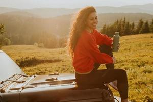 mujer joven relajándose en el capó de un vehículo de terreno en el campo foto