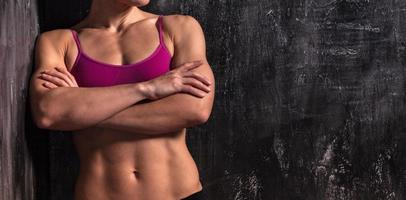 Strong muscular woman is posing against grunge wall photo