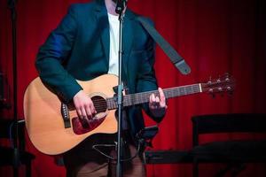 el hombre toca la guitarra clásica contra la cortina roja foto