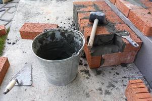 Bucket with a solute, trowel, rubber mallet and clay bricks photo