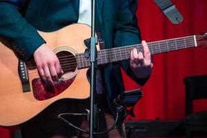 el hombre toca la guitarra clásica contra la cortina roja foto