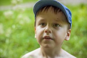 A cute blond boy experiences the joy of walking on a summer day by the river, sitting on the juicy grass. Funny facial expression. summer heat, a child without a T-shirt. photo