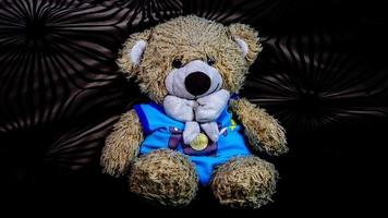 teddy bear in a blue t-shirt on a black sofa photo