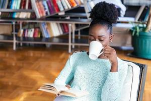 Cozy sofa and a beautiful girl, reading a book, concepts of home and comfort, place for text. Young pretty woman sitting and drinking coffee wile reading a book enjoys of rest photo