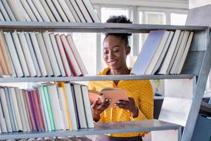 Woman African American college student working at library holding a book in hands, looking smart. bookshelves at the library. photo