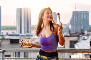 joven caucásica comiendo ensalada al aire libre al atardecer. dieta saludable. hermosa mujer sonriente comiendo ensalada vegetariana orgánica fresca. concepto de alimentación saludable, alimentación y estilo de vida. Salud y Belleza foto