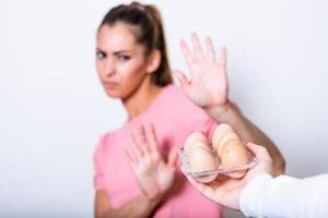 Woman refusing to eat eggs. Egg Free Affected Allergy Banned Restriction. Young beautiful woman holding fresh egg at home with open hand doing stop sign with serious and confident expression photo