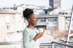 African American Woman drinking coffee on her balcony with a city view in the sun, outdoor in sunlight light, enjoying her morning coffee. photo