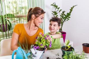 mamá y niño riegan las plantas juntos, la pequeña asistente de jardinero de mamá, cuida de los niños y las flores. chico lindo regando de la regadera, cuidando árboles y plantas, niño mojado foto