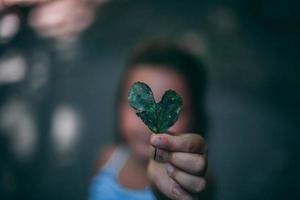 hoja en forma de corazón en el bosque sostenida por un niño lindo foto