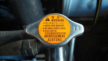 Car radiator cap with warning in many language, in english means translate never open when hot. photo