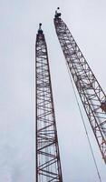 Portrait of two large crawler crane boom soaring at the sky. photo