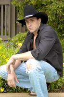 Handsome young cowboy crouches down for a masculine pose with his black cowboy hat. photo
