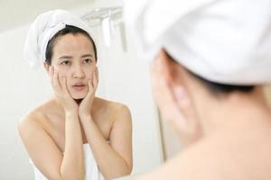 Problem skin. Concerned young asian women popping pimple on cheek while standing near mirror in bathroom. young asian women with acne photo