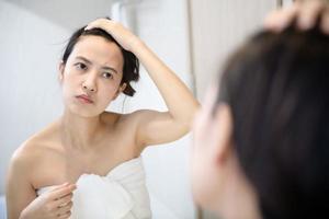 Problem skin. Concerned young asian women popping pimple on cheek while standing near mirror in bathroom. young asian women with acne photo