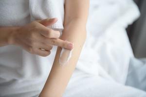 Asia woman sitting on bed and applying cream on body. photo