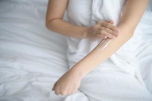 Asia woman sitting on bed and applying cream on body. photo