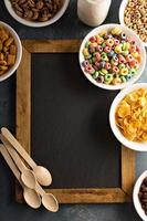 Variety of cold cereals in white bowls around chalkboard photo