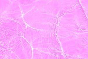 Defocus blurred transparent purple colored clear calm water surface texture with splashes and bubbles. Trendy abstract nature background. Water waves in sunlight with copy space. Pink water drop shine photo