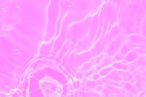 Defocus blurred transparent purple colored clear calm water surface texture with splashes and bubbles. Trendy abstract nature background. Water waves in sunlight with copy space. Pink water drop shine photo