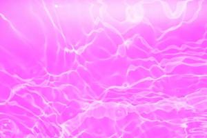 Defocus blurred transparent purple colored clear calm water surface texture with splashes and bubbles. Trendy abstract nature background. Water waves in sunlight with copy space. Pink water drop shine photo