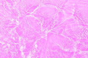 Defocus blurred transparent purple colored clear calm water surface texture with splashes and bubbles. Trendy abstract nature background. Water waves in sunlight with copy space. Pink water drop shine photo