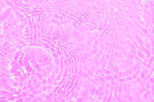 Defocus blurred transparent purple colored clear calm water surface texture with splashes and bubbles. Trendy abstract nature background. Water waves in sunlight with copy space. Pink water drop shine photo
