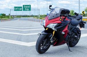 Red black motorcycle modern style parked on road with message Let's go Travel Trip on green roadsign background photo