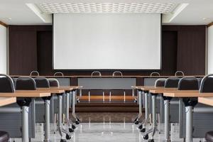 sala de seminarios con una mesa para oradores en medio del escenario y fondo de pantalla blanca foto