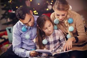 Family reading story book together under Christmas tree photo